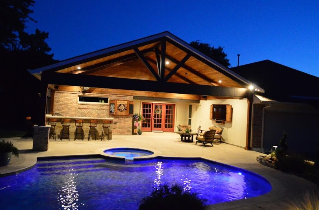 Outdoor lighting illuminating a residential pool and covered patio at dusk.